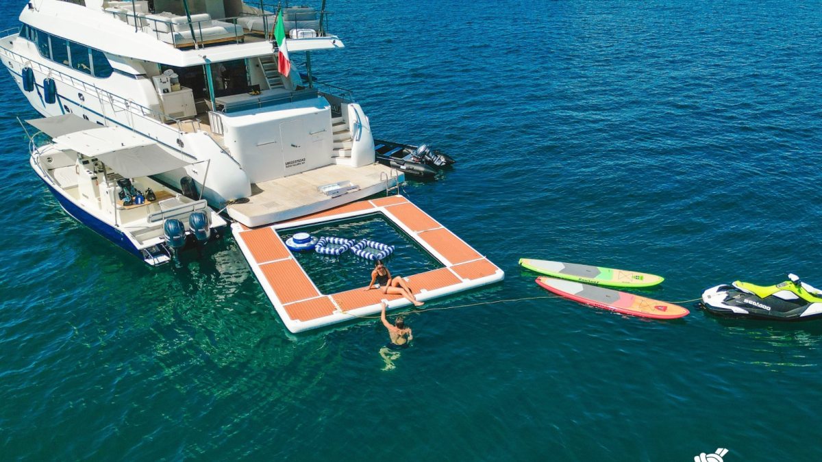 Guests swimming, paddleboarding and riding water toys beside a private yacht in turquoise water near Puerto Vallarta